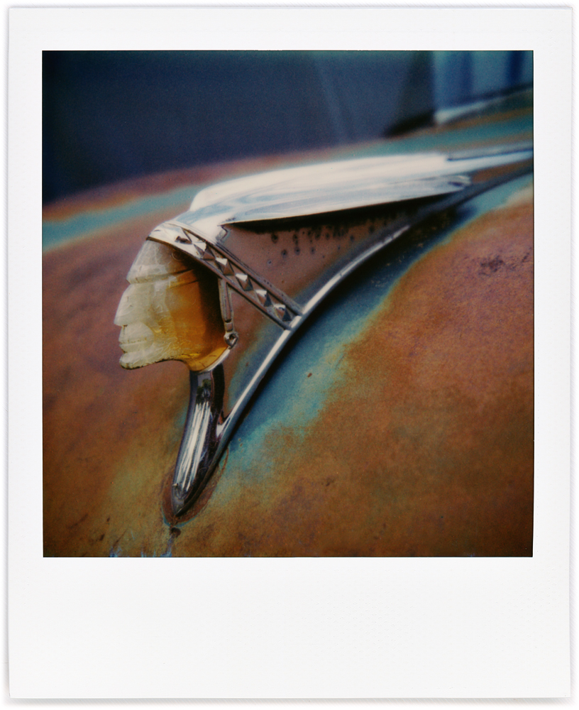 A Polaroid photo of a 1958 Pontiac Indian Head hood ornament.