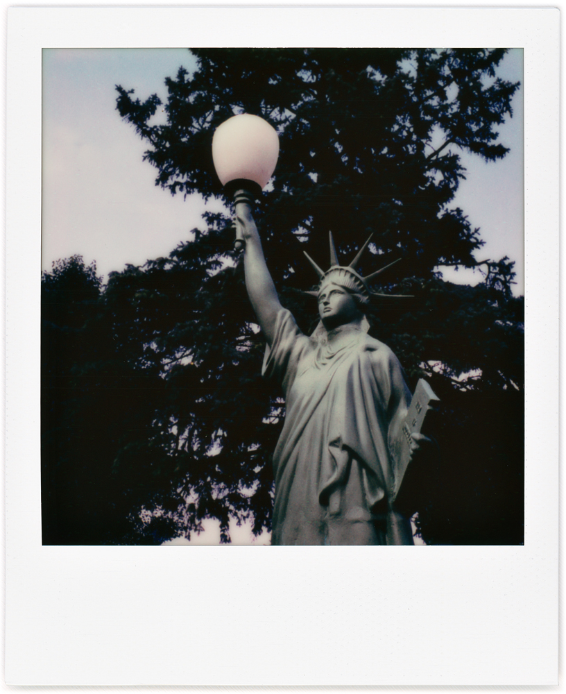 A Polaroid photo of the Statue of Liberty holding up a yard light in the small town of Ossian, Indiana. Made of cast aluminum by Tuscumbia Iron Works.