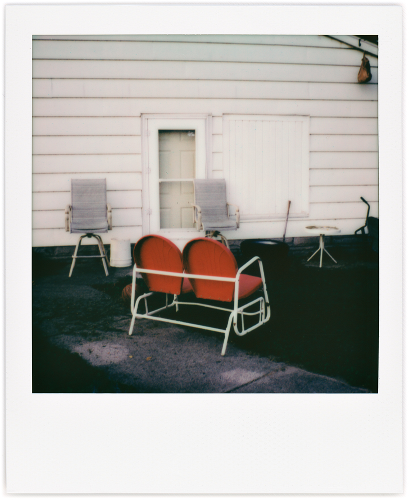 Polaroid photo of a red metal motel chair double-seat glider rocker.